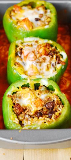 green peppers stuffed with meat and cheese sitting in a pan on top of a wooden table