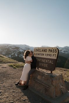 a man and woman kissing in front of the loveland pass sign on top of a mountain