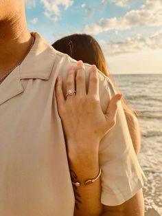 a man and woman standing next to each other on the beach with their arms around each other