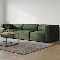 a green couch sitting on top of a wooden floor next to a table and chair