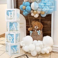 a teddy bear sitting on top of a basket next to balloons and blocks that spell out the word baby