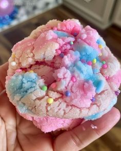 a hand holding a pink and blue sprinkled cookie