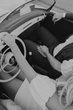 black and white photograph of a woman sitting in a car with her hands on the steering wheel