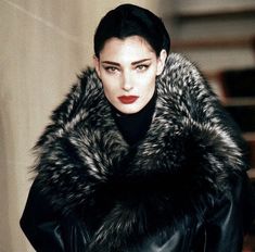 a woman wearing a black leather coat with a fur stole around her neck and red lips