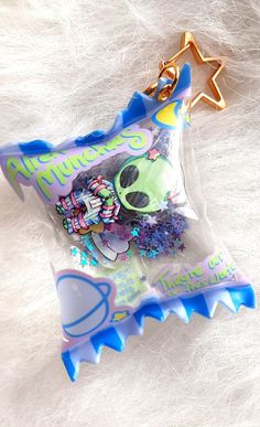 a keychain with an alien doll in it's plastic bag on top of white fur