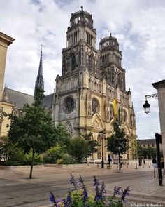 a large cathedral with tall spires towering over a city street filled with flowers and trees