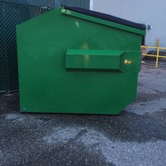 a large green trash can sitting in the middle of a parking lot next to a fence