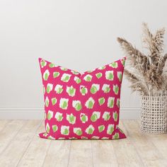 a pink and green pillow sitting on top of a wooden floor next to a potted plant