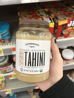 a person holding up a jar of tahitii in front of a store shelf