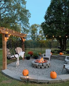 an outdoor fire pit surrounded by chairs and pumpkins with lights strung from the trees