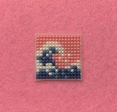 a small square beaded with an image of a surfer on the waves in blue and pink