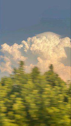 the sky is very cloudy and there are many trees in front of it, as seen from a moving train