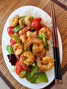 shrimp and vegetable stir fry with chopsticks on a white plate next to rice