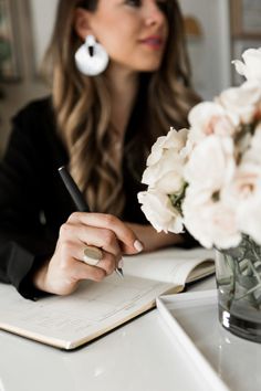 a woman sitting at a table writing on a notebook with flowers in front of her