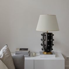 a lamp sitting on top of a white table next to a gray couch and pillows