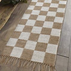 a brown and white checkered rug sitting on top of a wooden floor next to a potted plant