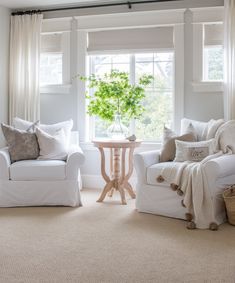 a living room with two white couches and a small table in front of the window