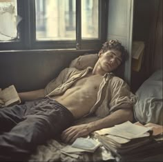 a shirtless man laying on top of a bed in a room with lots of papers