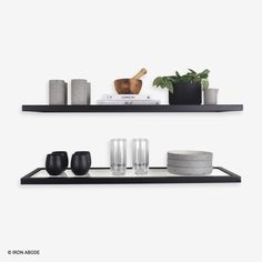 two black shelves with vases, candles and other items on them in front of a white wall