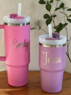 two pink and purple tumblers sitting on top of a wooden table next to each other