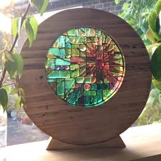 a stained glass piece sitting on top of a wooden stand in front of a window