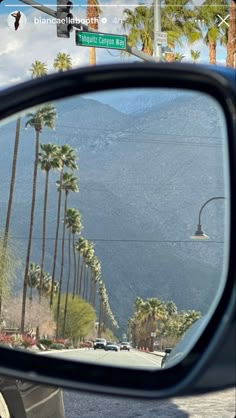 the side mirror of a car with palm trees and mountains in the background