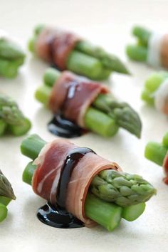 asparagus wrapped in bacon and sauce on a white surface with other food items