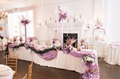 the tables are decorated with purple and white flowers, ribbons, and candles for an elegant wedding reception