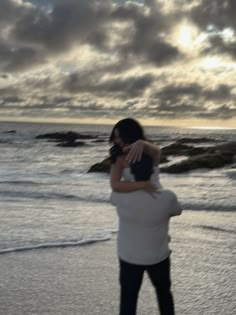 a woman carrying a man on her back while walking along the beach at sunset with clouds in the background