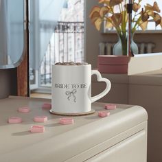 a white coffee mug with pink marshmallows on it sitting on top of a dresser