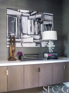 a painting on the wall above a table with books and a lamp in front of it