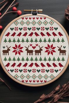 a cross stitch christmas pattern with reindeers and holly leaves on it, next to some red berries