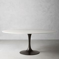 an oval white marble dining table with black metal base and round, circular shaped top