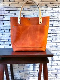 These beautiful totes are one of a kind timeless classics. They are all made with 100% genuine leather ranging from 3-5 oz. All exterior seams are double stitched. This adorable bag measures approx. 10 1/2" tall, approx. 12 1/2" across the top, approx. and has a depth of approx. 5".  The handles have an approx. drop of 5". You can pick to have handles or no handles, snap or no snap, handle color and fastener color. I do not include the cross-body strap.  I use real leather for all my items, whic Orange Leather Tote Bag, Handmade Leather Bag With Double Handle, Orange Leather Bucket Bag, Orange Leather Satchel With Leather Handles, Orange Leather Tote Satchel, Orange Leather Shoulder Bag For Everyday, Orange Leather Satchel For Everyday Use, Everyday Orange Leather Shoulder Bag, Handmade Leather Tote Satchel