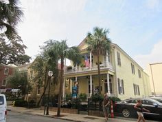 two people are walking down the street in front of a yellow house with palm trees