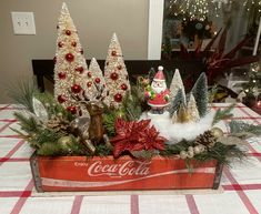 a coca - cola crate filled with christmas trees and other decorations on top of a table