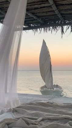 a sailboat sitting on the beach under a covered area near the ocean at sunset