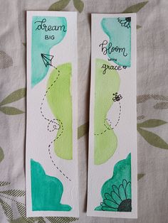 two bookmarks with watercolors on them sitting on top of a table cloth