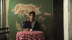 a man sitting at a table with a red and white checkered table cloth on it