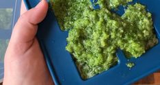 a blue plate topped with green food on top of a wooden table next to a person's hand