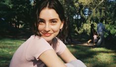 a woman sitting in the grass with her arms crossed and smiling at the camera,