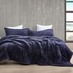 a bed covered in a blue blanket next to a window