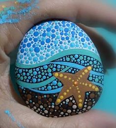 a hand holding a painted rock with a starfish on it