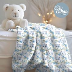 a white teddy bear sitting on top of a bed next to a blue and green blanket