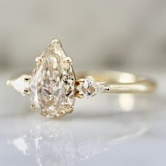 an oval cut diamond ring with three pear shaped diamonds on the band, set in yellow gold