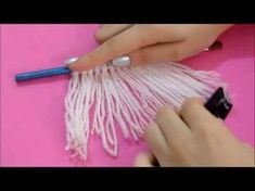 someone is doing something with yarn on a pink surface and holding a blue handled brush