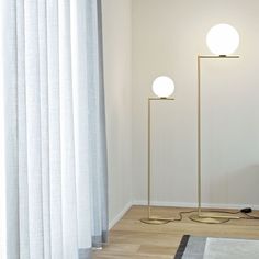 two floor lamps sitting next to each other on a hard wood floor in front of a white curtain