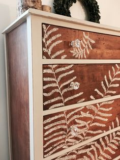 an old dresser has been painted with gold leaf stencils and is next to a wreath