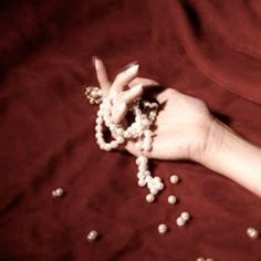 a woman's hand holding beads and making the peace sign with her fingers on a red blanket