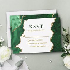 a green and gold marbled wedding card with white flowers on the table next to it